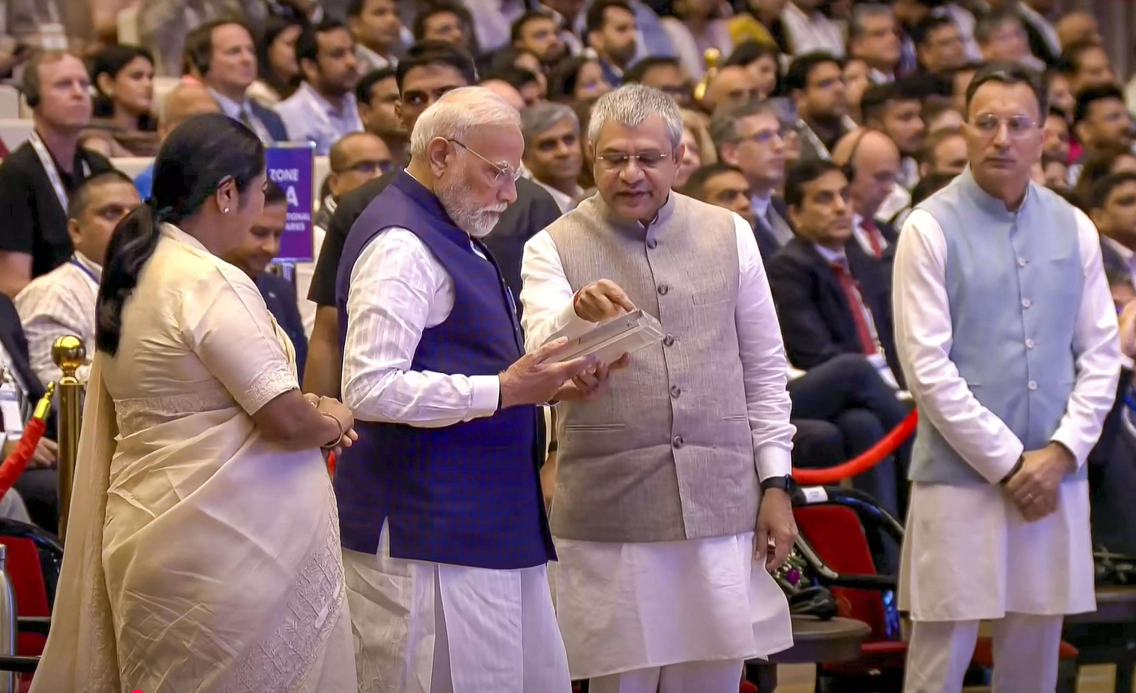 सेमिकॉन इंडिया 2025 में बोलते हुए प्रधानमंत्री नरेंद्र मोदी की क्लोज-अप फोटो वाला एक ग्राफिक। जिसमें एक बड़े सफेद टेक्स्ट बॉक्स में उनका उद्धरण लिखा है: 'तेल को ब्लैक गोल्ड कहा जाता था... लेकिन चिप्स डिजिटल डायमंड हैं।' नीचे लिखा है: 'पीएम मोदी सेमिकॉन इंडिया 2025 में, 2 सितंबर 2025'। बैकग्राउंड में नीले रंग का डॉट्स पैटर्न है।

"एक कार्यक्रम के दौरान प्रधानमंत्री नरेंद्र मोदी, केंद्रीय मंत्री अश्विनी वैष्णव से पहला मेड-इन-इंडिया चिप प्राप्त कर रहे हैं। मंच पर और भी कई लोग खड़े हैं और पीछे दर्शक दीर्घा में लोग बैठे हुए हैं।"
